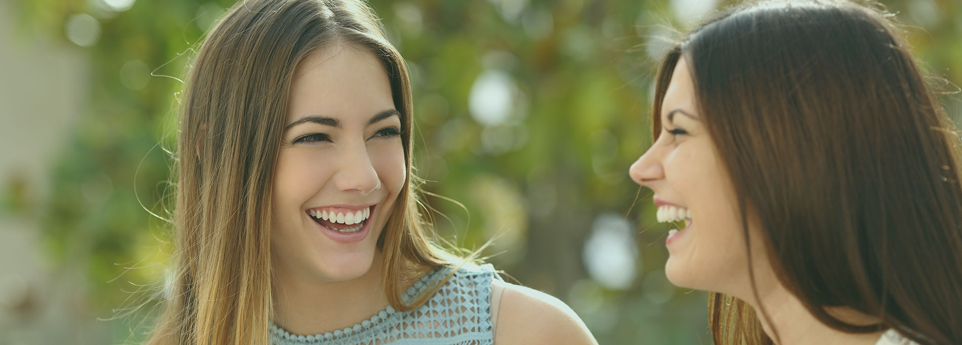 Two women with beautiful teeth smiling happily at each other