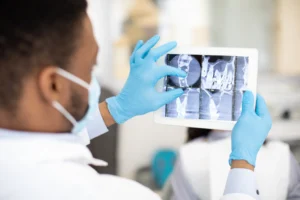 Clinician in a face mask reviewing dental X-rays on a tablet